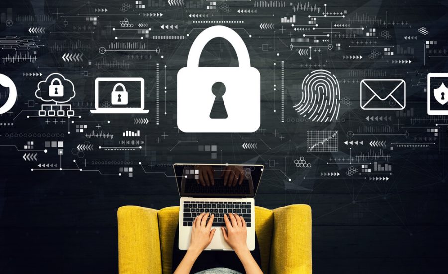 Personne tapant sur un ordinateur portable sur une chaise jaune, avec un grand cadenas et des icônes de sécurité numérique flottant au-dessus, illustrant la cybersécurité.